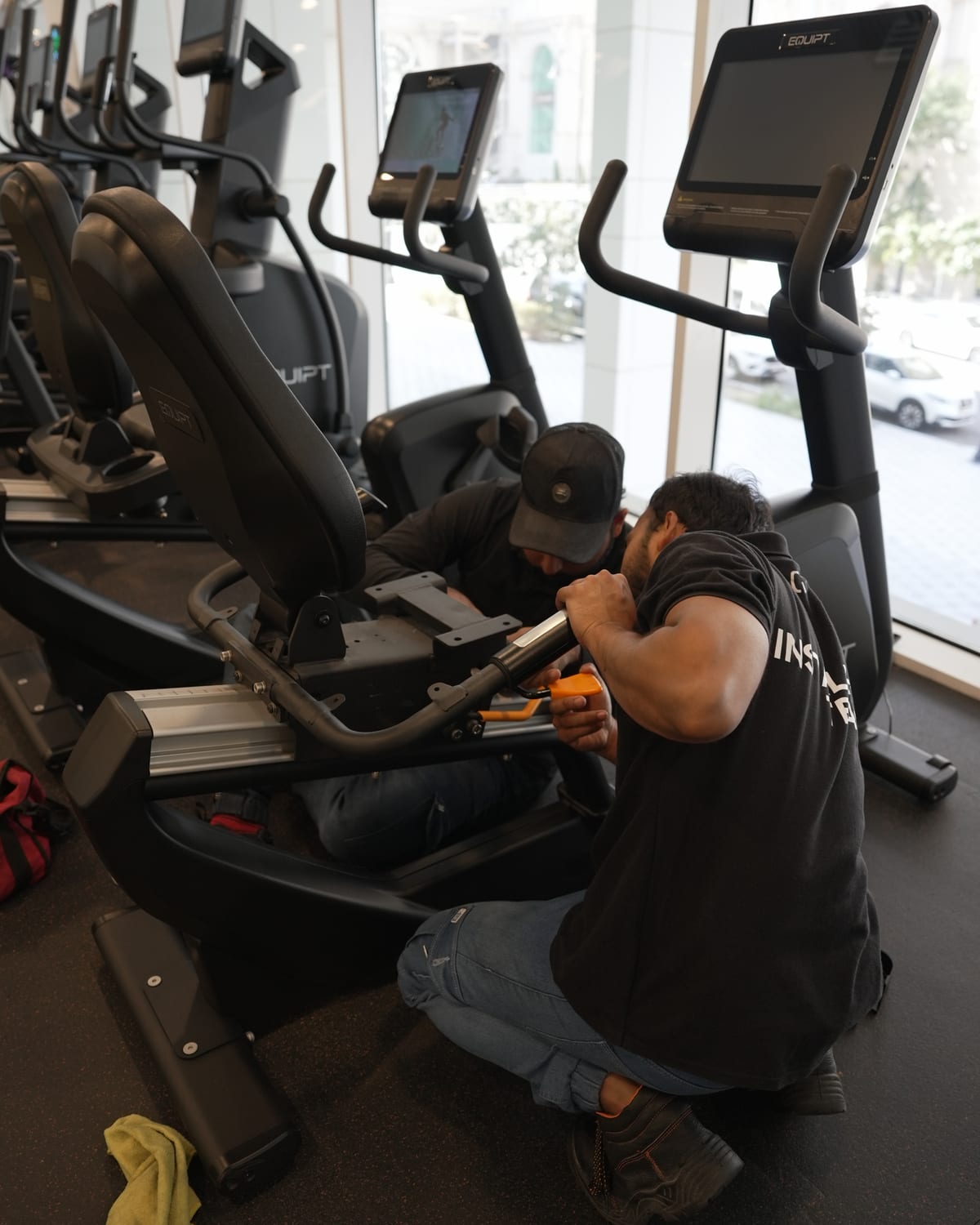 An Equipt engineer working underneath a cross-trainer beside a curtain wall.